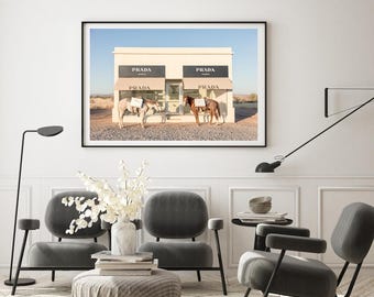 May include: A photograph of a desert landscape with two horses wearing saddles and bags in front of a building with the word "PRADA" on the front. The building has a light brown facade and a white awning. The horses are facing each other and the sky is blue.