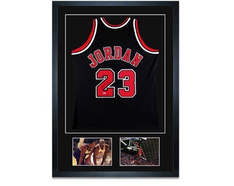 May include: A framed black basketball jersey with the name "JORDAN" and the number "23" in red on the back. The frame includes two smaller photos of Michael Jordan playing basketball.