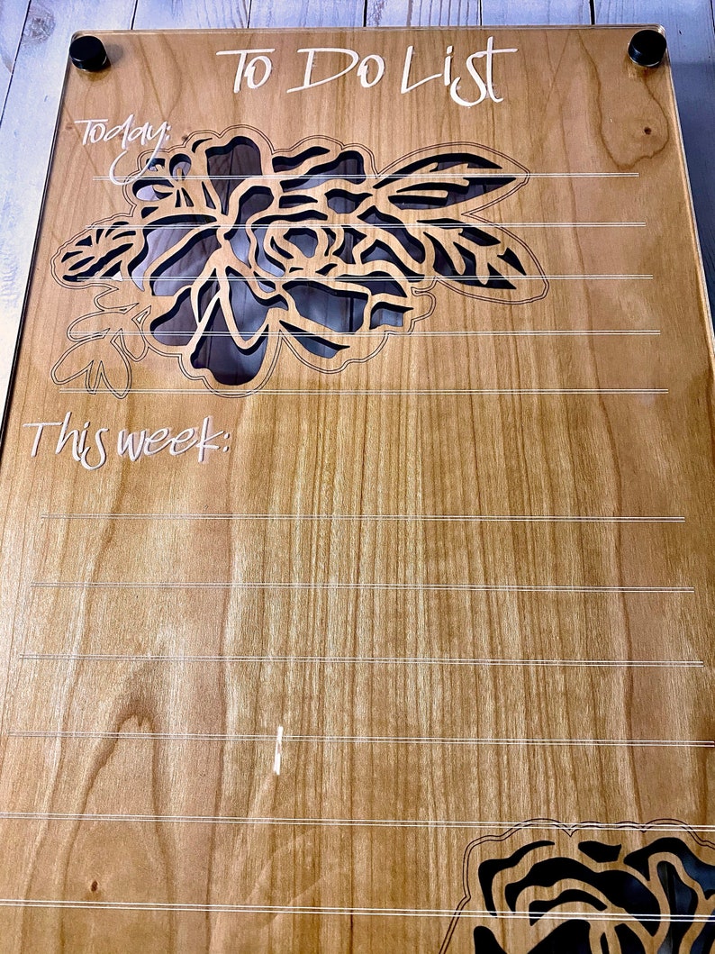Puede incluir: Un tablero de madera para lista de tareas con un dise&ntilde;o floral. El tablero tiene una inscripci&oacute;n blanca que dice "To Do List". El tablero est&aacute; dividido en dos secciones, una para "Hoy" y otra para "Esta semana".