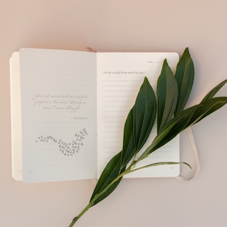 May include: A white journal with a quote by Mary Oliver on the left page and a lined page on the right. The quote reads "You will survive and you will find purpose in the chase. Moving on doesn't mess letting go." A green branch with leaves is placed on top of the journal.