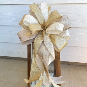 May include: A gold and white Christmas bow with a burlap ribbon, tied on a wooden lantern.