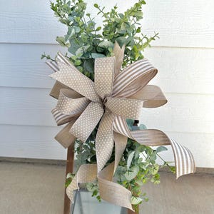 May include: A brown lantern with a green eucalyptus garland and a brown bow with white polka dots and stripes.