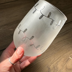 May include: A frosted glass wine glass with a design of white string lights on the side.
