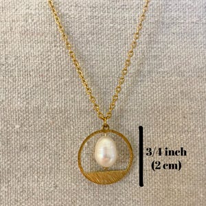 May include: A gold chain necklace with a gold circle pendant featuring a white pearl. The pendant has a textured, brushed gold finish. The pearl is approximately 3/4 inch (2 cm) in diameter.