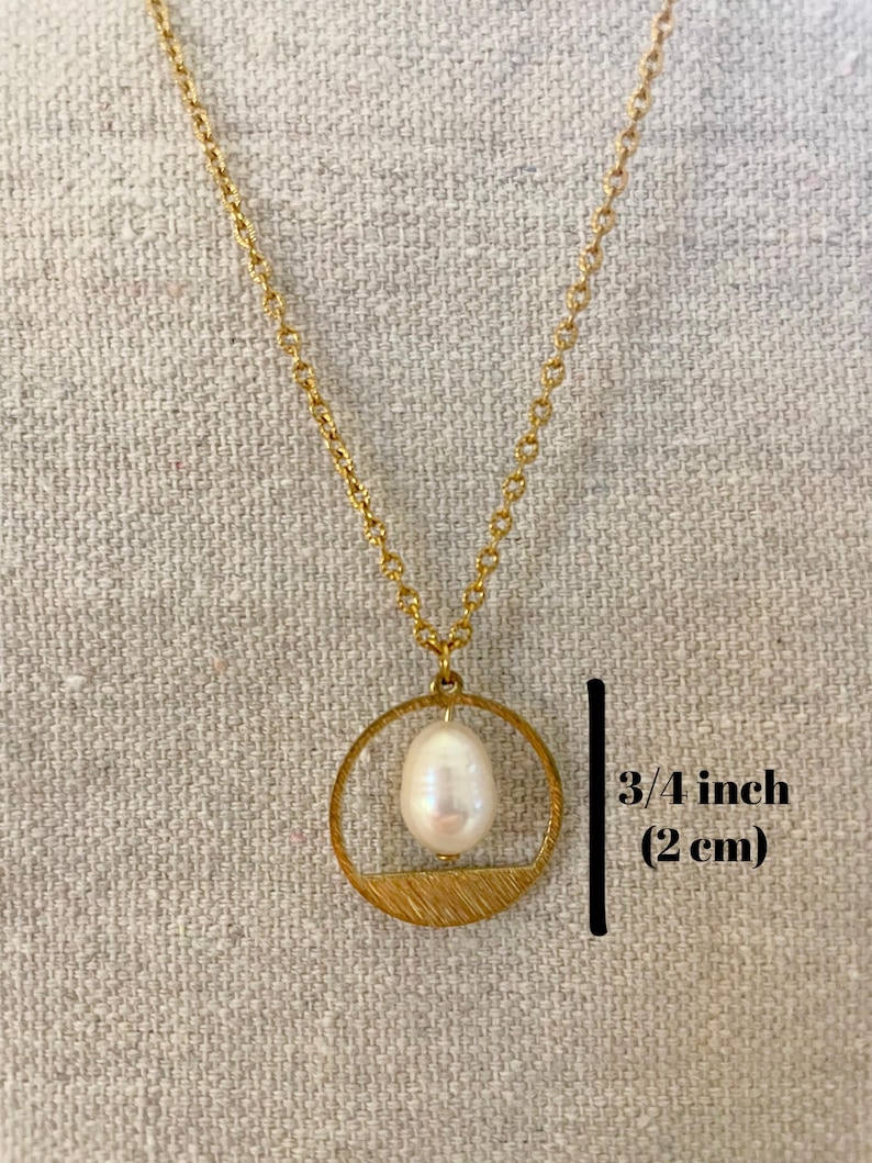 May include: A gold chain necklace with a gold circle pendant featuring a white pearl. The pendant has a textured, brushed gold finish. The pearl is approximately 3/4 inch (2 cm) in diameter.