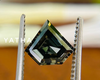 Könnte beinhalten: Ein dunkelgrüner Edelstein mit quadratischer Form und facettenreichem Schliff. Der Edelstein wird von einer Pinzette gehalten.