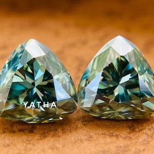 May include: Two triangular green gemstones with a star-like pattern inside. The gemstones are faceted and have a light blue hue.
