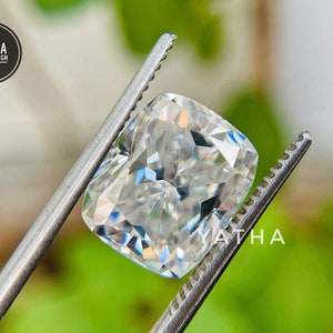May include: A clear, cushion-cut gemstone held by tweezers. The gemstone is a brilliant white with many facets.
