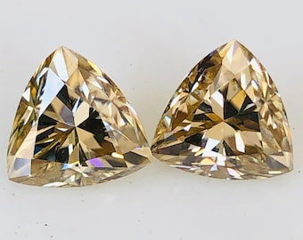Puede incluir: Dos piedras preciosas triangulares, facetadas, de color marrón claro con un tono dorado.