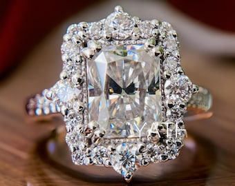 May include: A silver ring with a large, rectangular, clear diamond surrounded by a halo of smaller diamonds. The ring has a delicate, ornate design with a scalloped edge.