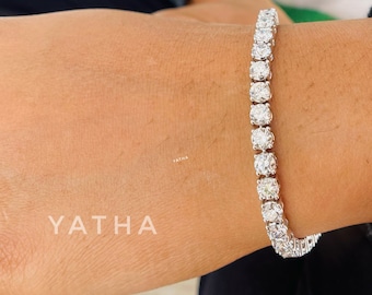 May include: A silver tennis bracelet with round, clear stones. The bracelet is on a person's wrist.