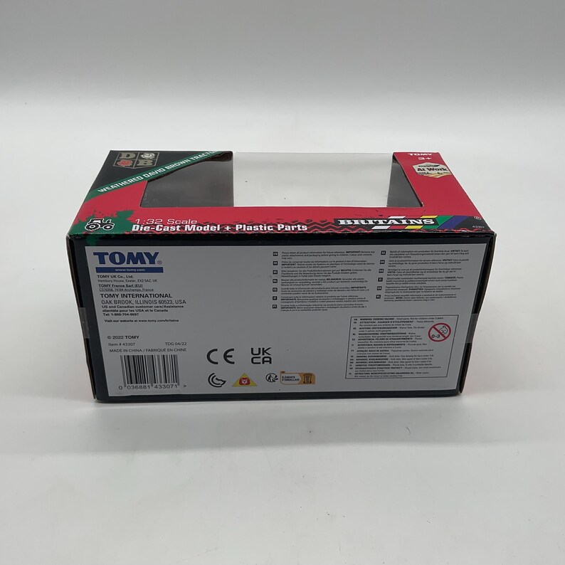 May include: A TOMY die-cast model box with a clear plastic window. The box is black with red and green accents and features the text "1:32 Scale Die-Cast Model + Plastic Parts". The box also includes the TOMY and Britains logos.