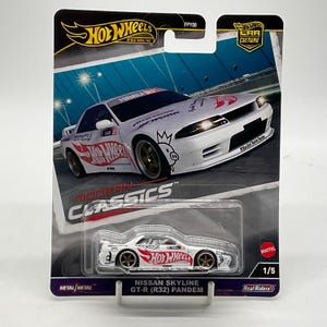May include: A Hot Wheels Premium Nissan Skyline GT-R (R32) Pandem die-cast car in white with red Hot Wheels branding and gold wheels. The car is packaged in a blister card featuring a graphic of the vehicle on a track with Modern Classics text.