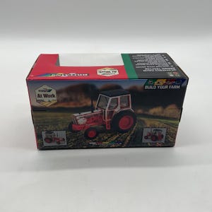 May include: A boxed toy tractor, predominantly red and white, with black accents. The box features the text "At Work" and "Build Your Farm". The tractor model is a weathered David Brown.