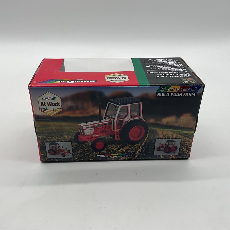 May include: A boxed toy tractor, predominantly red and white, with black accents. The box features the text "At Work" and "Build Your Farm". The tractor model is a weathered David Brown.