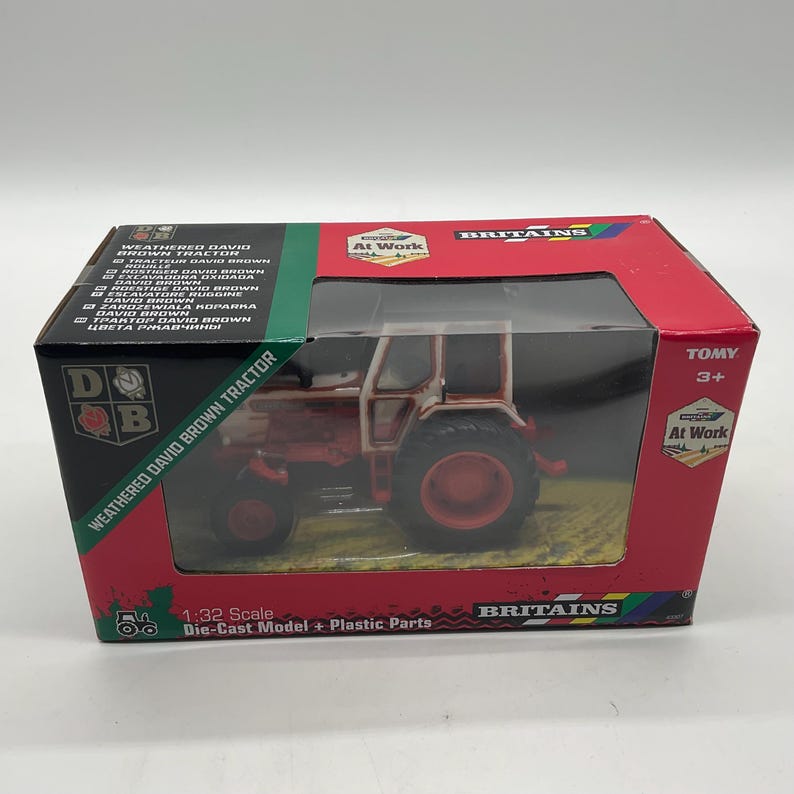 May include: A boxed 1:32 scale die-cast model of a weathered David Brown tractor. The toy tractor is red and white, with black tires, and is displayed in a red and black box with the Britains logo.