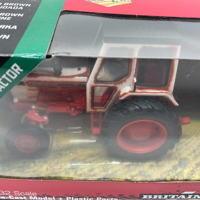 May include: A die-cast model tractor with a red and white color scheme. The tractor features large black tires with red rims and a detailed cabin. The model is labeled "DAVID BROWN" and is a 1:32 scale replica.