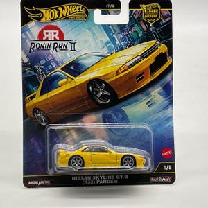 May include: A Hot Wheels Premium die-cast Nissan Skyline GT-R (R32) Pandem toy car in yellow, packaged in a blister card featuring Ronin Run II branding, a city street graphic, the Hot Wheels logo, and the text 1/5, Metal/Metal, and Real Riders.