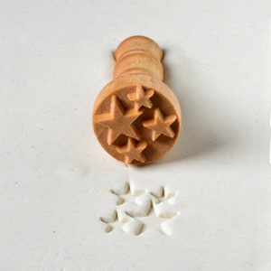 May include: A wooden stamp with a handle and a star-shaped design. The stamp is used to create impressions in clay or dough.
