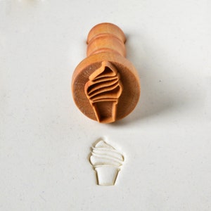 May include: A wooden ice cream cone stamp with a brown handle. The stamp is used to create an impression of an ice cream cone in clay or dough.
