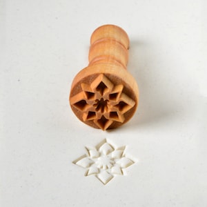 May include: A wooden stamp with a detailed starburst design. The stamp is used to create an impression in clay or dough.