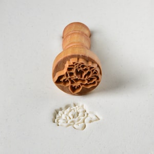 May include: A wooden flower-shaped cookie stamp with a detailed design. The stamp is used to create a flower impression in dough or fondant.