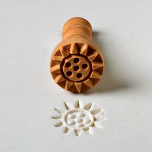 May include: A wooden stamp with a starburst design and six circular indentations. The stamp is used to create a decorative imprint on a surface.