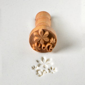 May include: A wooden stamp with a floral design. The stamp is used to create an impression in clay or dough.