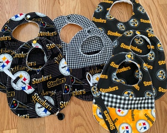 May include: Five black and yellow baby bibs with the Pittsburgh Steelers logo and the word "Steelers" printed on them. The bibs are made of a soft, absorbent fabric and have a snap closure.