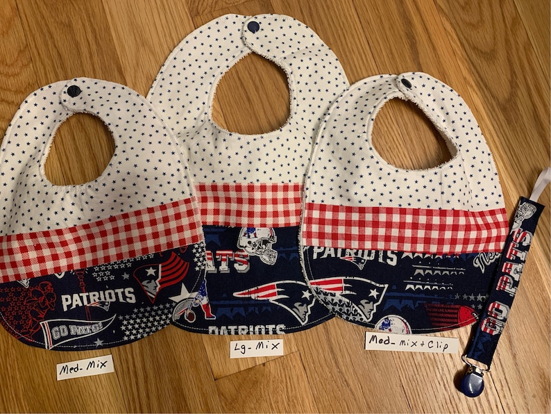 May include: Three baby bibs with a red and white checkered pattern and a blue and white Patriots themed fabric. The bibs are labeled "Med. Mix", "Lg. Mix", and "Med. Mix + Clip".