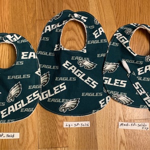 May include: Three green and white baby bibs with a Philadelphia Eagles pattern. The bibs are labeled "Med - SP - Solid", "Lg - SP - Solid", and "Med - SP - Solid + clip".