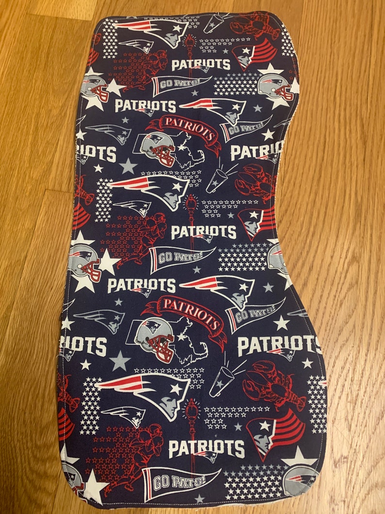 May include: A blue fabric with a white border featuring a repeated pattern of red, white, and blue American football helmets, stars, and the words "Patriots" and "Go Pats!"