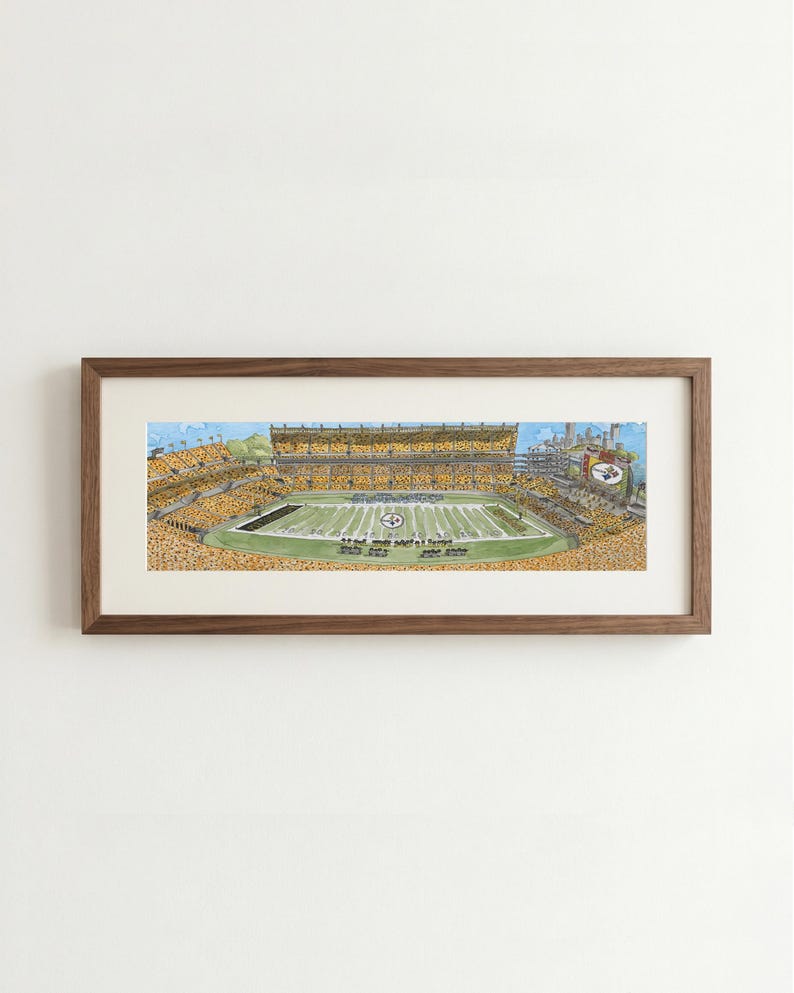 May include: A panoramic watercolor illustration of a football stadium filled with spectators wearing yellow and black, framed in a dark wood frame. The field is green with white yard lines and a central logo, under a light blue sky.
