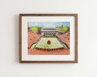 Könnte beinhalten: Ein gerahmter Aquarelldruck, der ein Footballstadion mit orangefarbenen Sitzplätzen, einem grünen Spielfeld und dem Text OKLAHOMA STATE in der Endzone zeigt. Das Stadion hat ein großes Gebäude im Hintergrund und ein Tor in der Mitte.