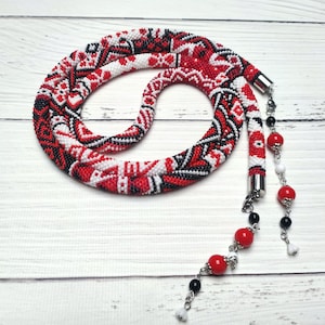 May include: A red, white, and black beaded necklace with a geometric pattern. The necklace has a long, dangling tassel with red, white, and black beads.