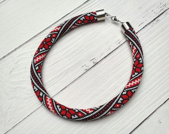 May include: A red, white and black beaded necklace with a geometric pattern. The necklace is made of small beads and has a silver clasp.