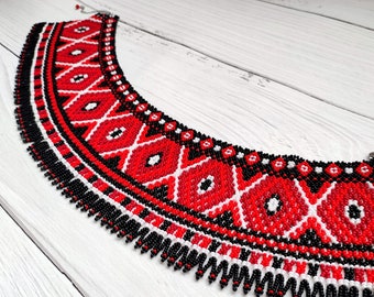 May include: A beaded necklace with a geometric pattern in red, white, and black. The necklace features a wide collar design with a fringe of beads along the bottom edge. The intricate beadwork creates a striking visual effect.