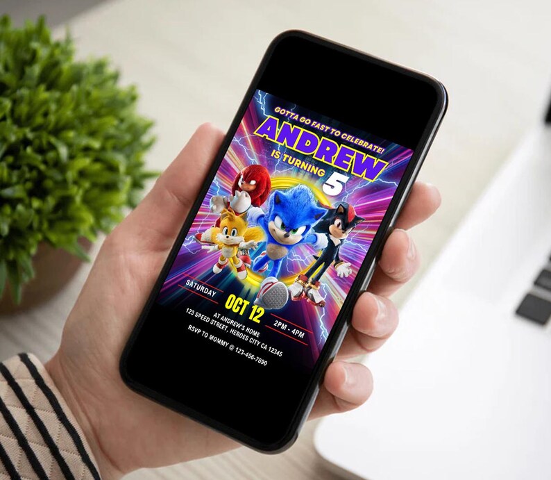 May include: A smartphone displays a colorful birthday invitation featuring Sonic the Hedgehog and friends. The invitation reads "Andrew is turning 5" with event details: Saturday, Oct 12, 2 PM-4 PM, at 123 Speed Street, Heroes City, CA. RSVP to Mommy.