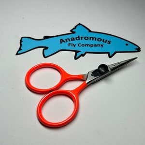 May include: Orange handled fly tying scissors with a silver blade. The scissors are on a white surface with a blue fish logo that says "Anadromous Fly Company".
