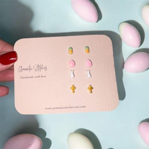 May include: A selection of six pairs of earrings on a pink card. The earrings feature carrot, egg, bunny, and cross designs. The card is printed with the text "Aromatic Stitches" and "Handmade with love" and the website address www.aromaticstitches.etsy.com.