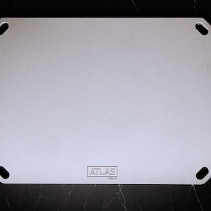 May include: A silver metal cutting board with rounded corners and four holes. The board has the word "ATLAS" printed in black on the bottom.