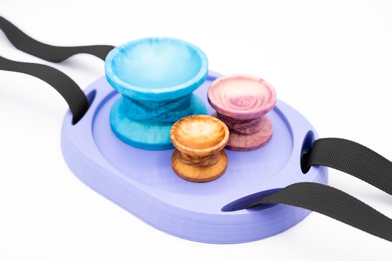 May include: A purple tray with two black straps, holding three small bowls. One bowl is blue, one is pink, and one is brown.