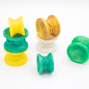 May include: Five colorful yo-yos, two green, one yellow, one gold, and one white. The yo-yos are made of plastic and have a variety of designs.