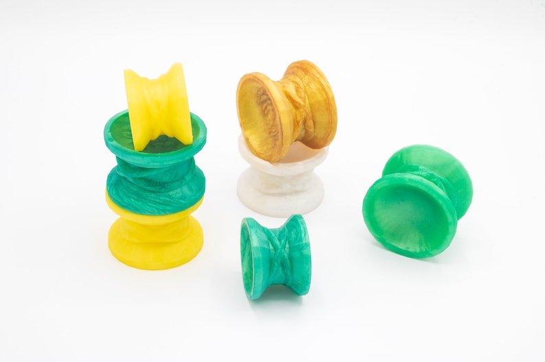 May include: Five colorful yo-yos, two green, one yellow, one gold, and one white. The yo-yos are made of plastic and have a variety of designs.