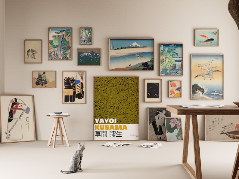 May include: A white wall gallery with a variety of framed prints, including Japanese woodblock prints, abstract art, and a poster with the text "YAYOI KUSAMA  草間彌生". The gallery is decorated with a wooden table, a small wooden stool, and a cat.