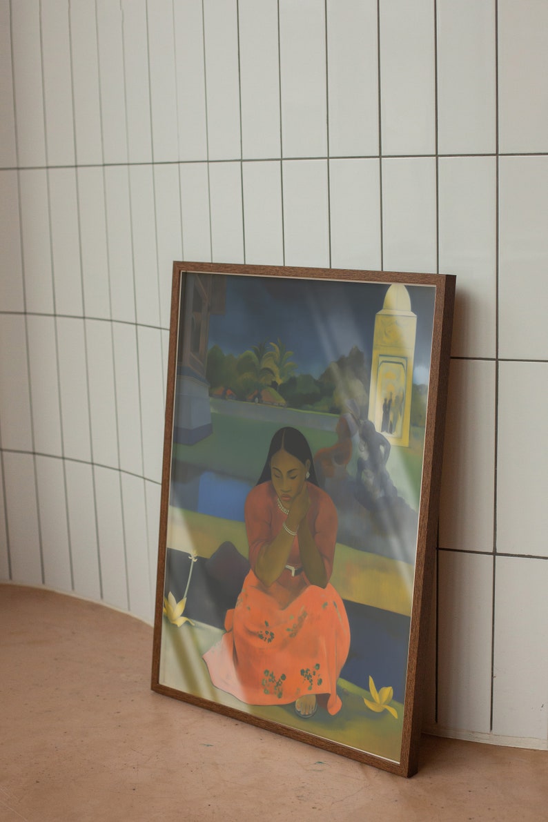 Peut inclure: Une peinture encadr&eacute;e repr&eacute;sentant une femme en robe rouge assise dans un paysage tropical. La femme regarde vers le bas et ses mains sont jointes sur ses genoux. La peinture est plac&eacute;e contre un mur en carrelage blanc.