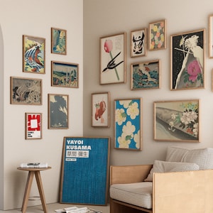 May include: A wall gallery featuring a variety of framed prints, including Japanese woodblock prints, abstract art, and a poster with Japanese text. The prints are arranged in a grid pattern and are hung on a white wall. A brown leather armchair and a small wooden table are in the foreground.