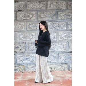 May include: A long-sleeved black top with a button-down front and a high neckline, paired with wide-leg trousers featuring a light-colored, intricate floral pattern. The ensemble consists of a dark solid-colored shirt and loose-fitting patterned pants.