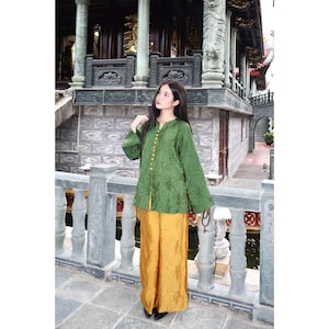 May include: A long-sleeved green blouse with a mandarin collar and a vertical row of gold buttons, paired with wide-leg mustard yellow trousers. Both garments feature a subtle, tonal jacquard pattern throughout the fabric, creating a textured look.