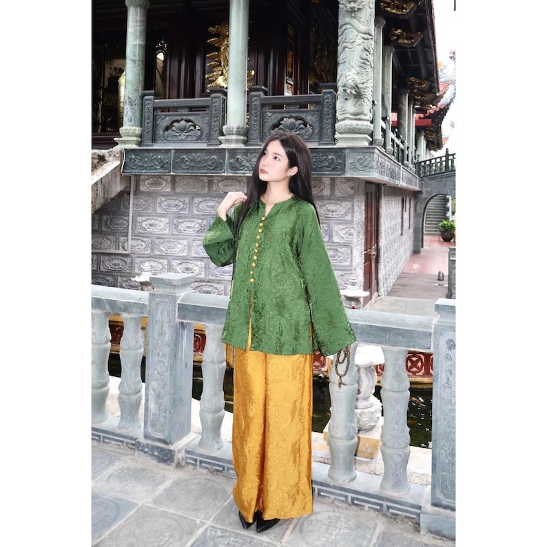 May include: A long-sleeved green blouse with a mandarin collar and a vertical row of gold buttons, paired with wide-leg mustard yellow trousers. Both garments feature a subtle, tonal jacquard pattern throughout the fabric, creating a textured look.